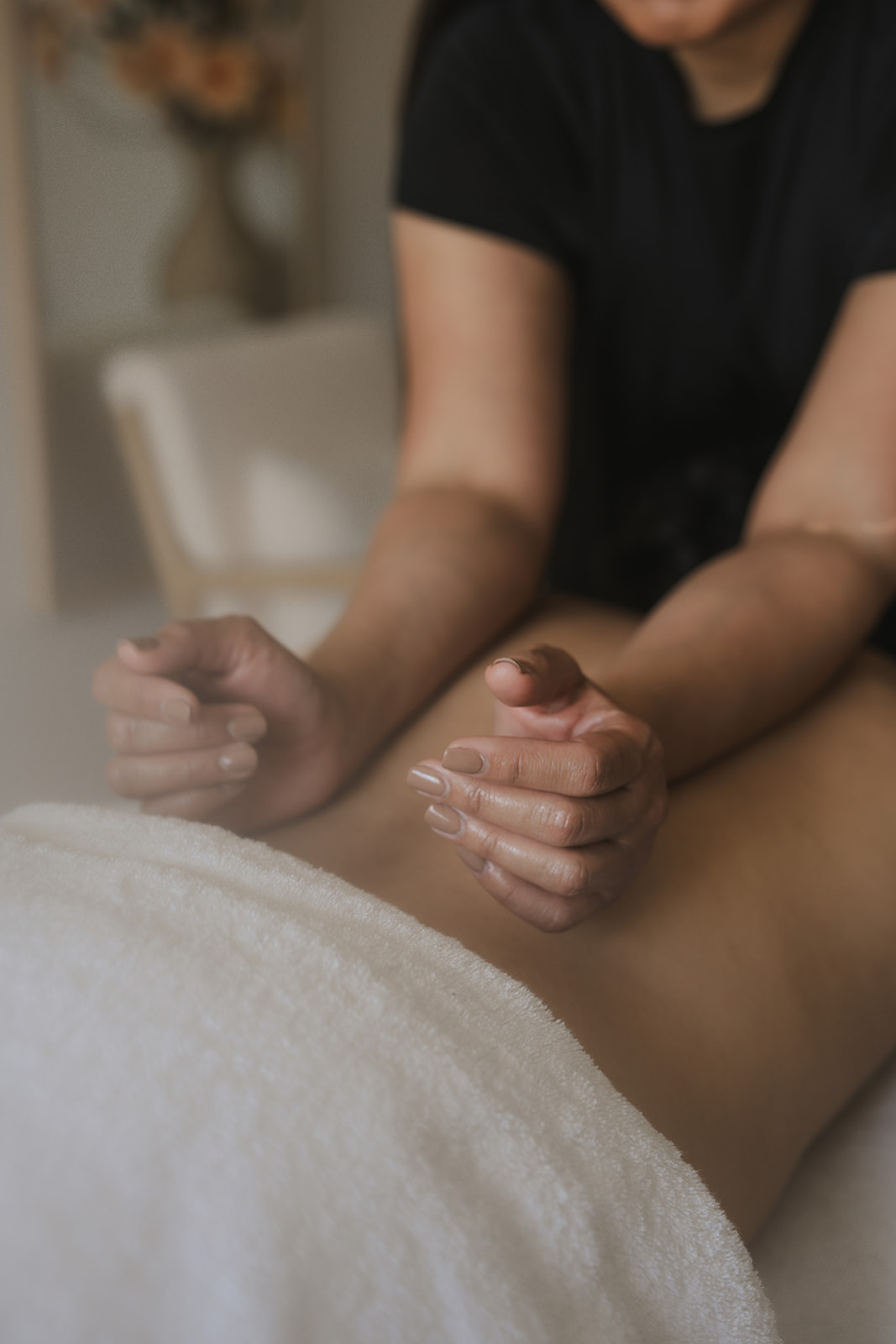 Handen van een masseur die de rug masseert op een zachte handdoek, warme spa-sfeer, onscherpe achtergrond.