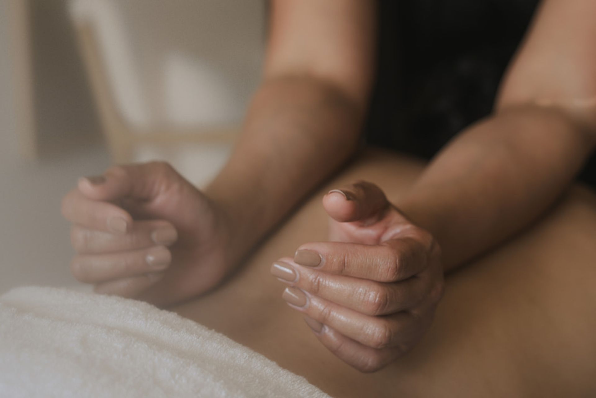 Handen die voeten masseren op een zachte handdoek, met warme, onscherpe achtergrond en ontspannen sfeer.