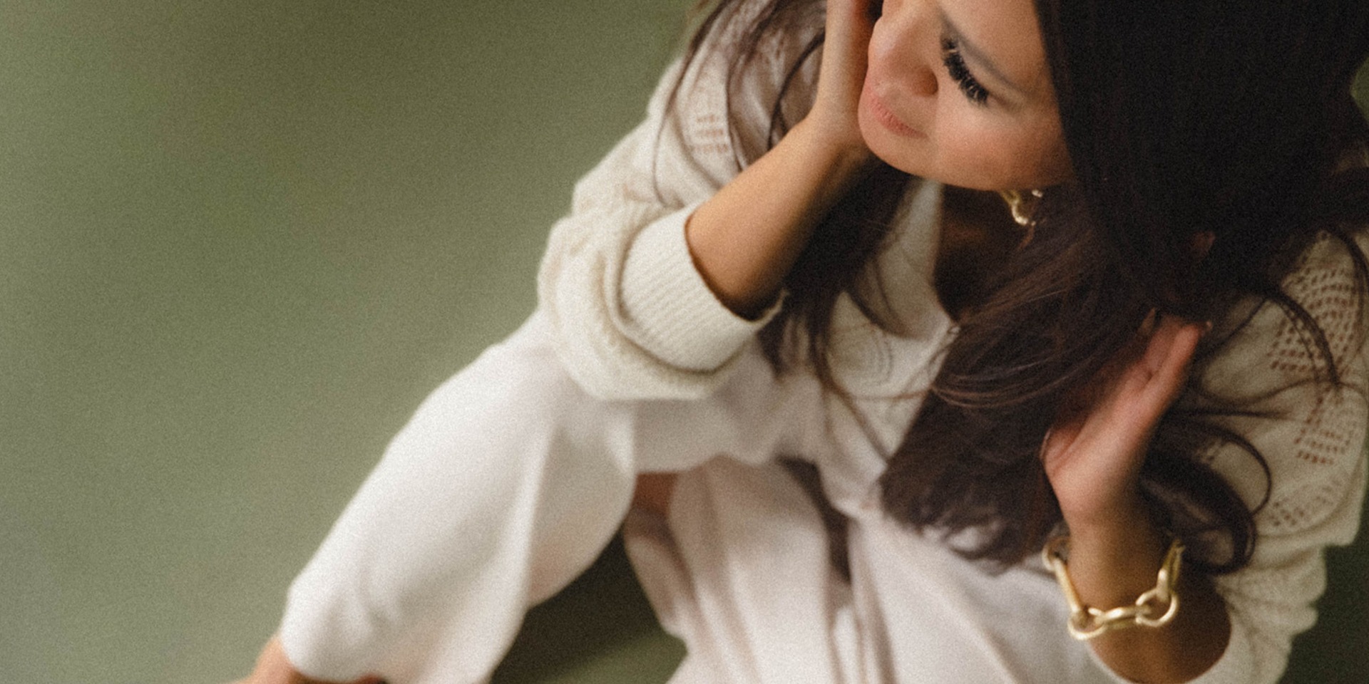 Vrouw met lange haren in witte blouse, leunt tegen een andere persoon, warme close-up met groene achtergrond.