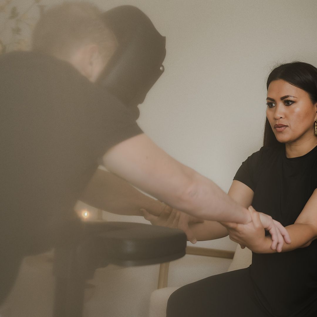Vrouw in zwarte kleding masseert iemands hand en pols, zachte close-up met onscherpe achtergrond.